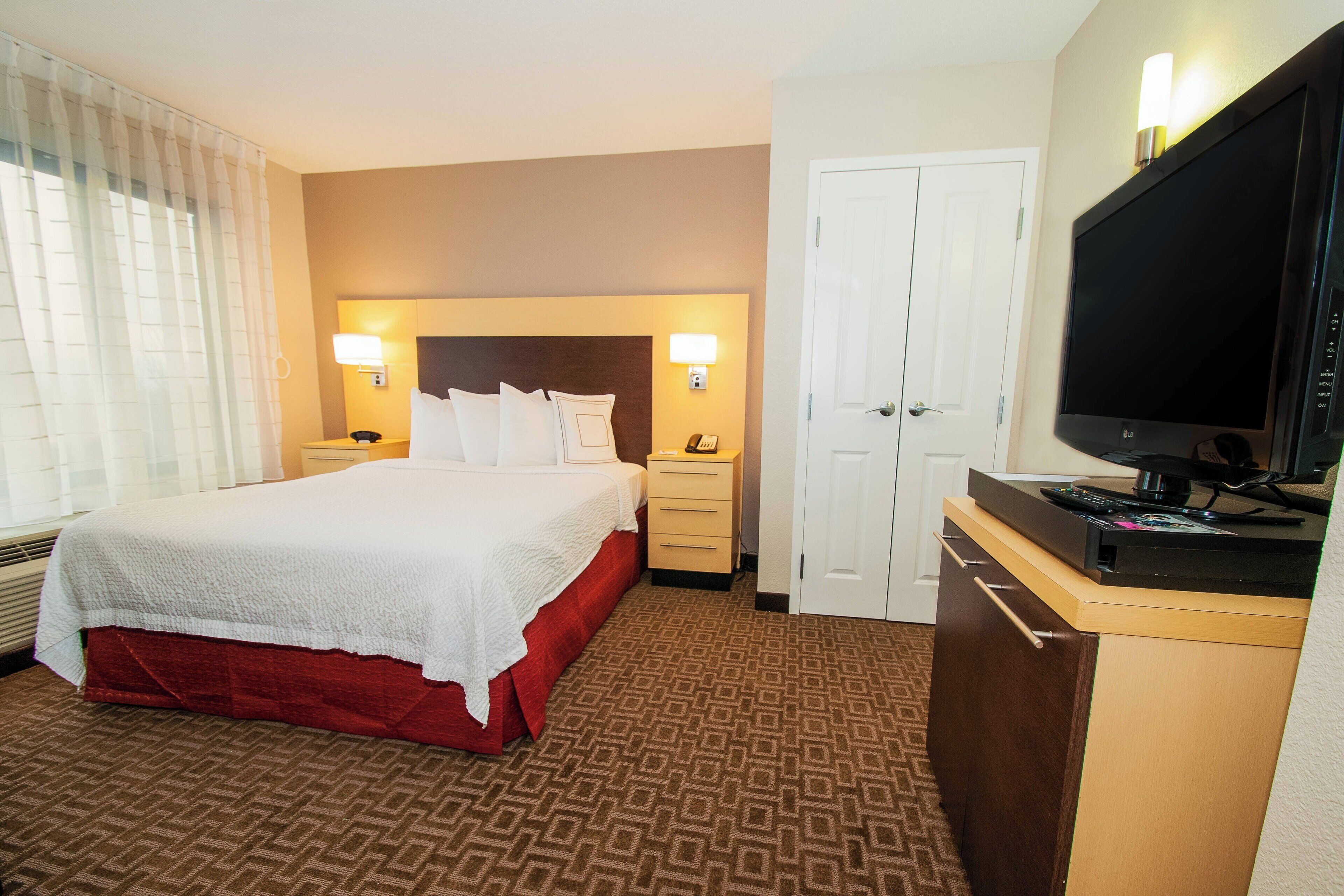 A hotel room with a large bed, bedside tables with lamps, a television, and a wardrobe.