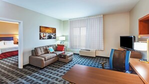 Een hotelkamer met een bed, een bank, een bureau met een computer, een televisie en een raam met gordijnen.