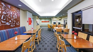Een restaurantgedeelte in een hotel met zitjes en tafels, een receptiebalie en een wand met kunstwerken.