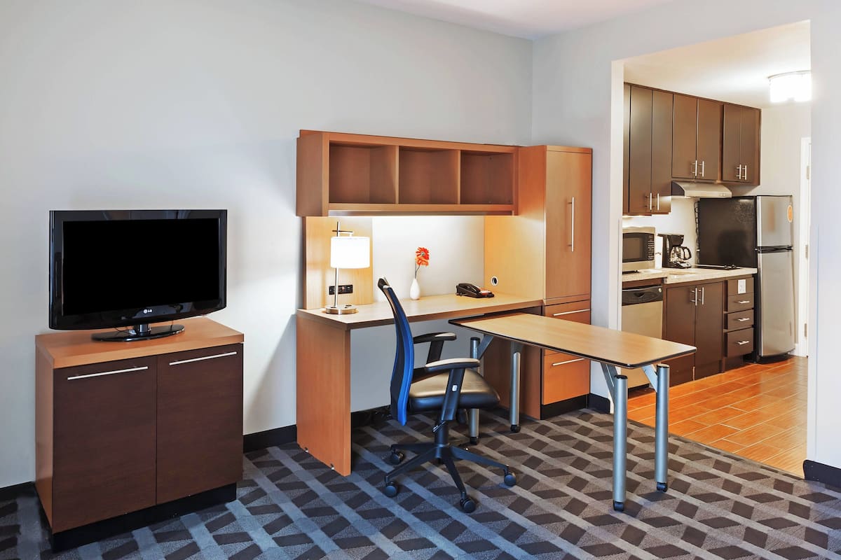 Une chambre d’hôtel compacte équipée d’une télévision, d’un bureau, d’une chaise, d’une kitchenette et dotée d’un sol à motifs.