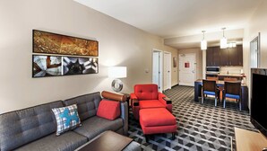 Een hotelkamer met een bank, een rode fauteuil, een eettafel met stoelen, een televisie en een kitchenette.