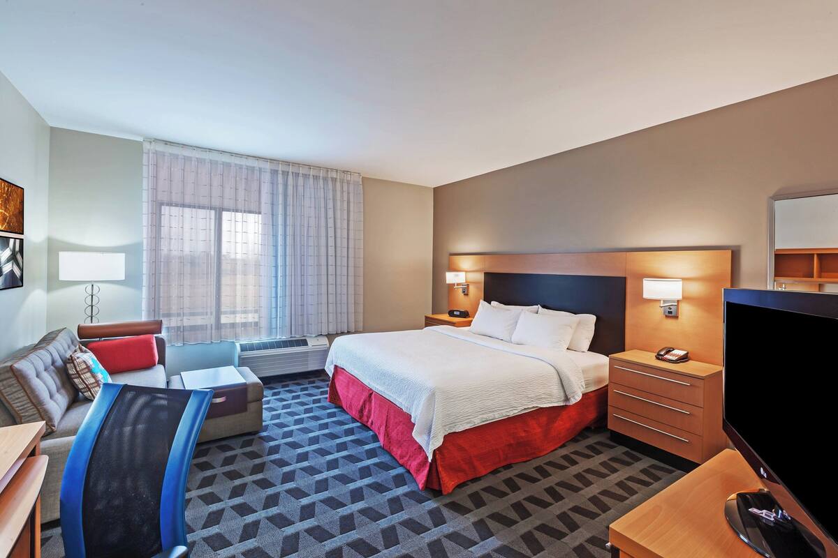 Une chambre d’hôtel comprenant un lit, une table de chevet, une télévision et un bureau avec une chaise.