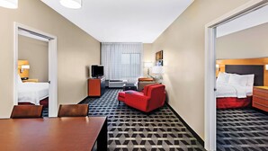 Een hotelkamer met een bed, een rode fauteuil, een houten tafel, een televisie en een bureau met een lamp.