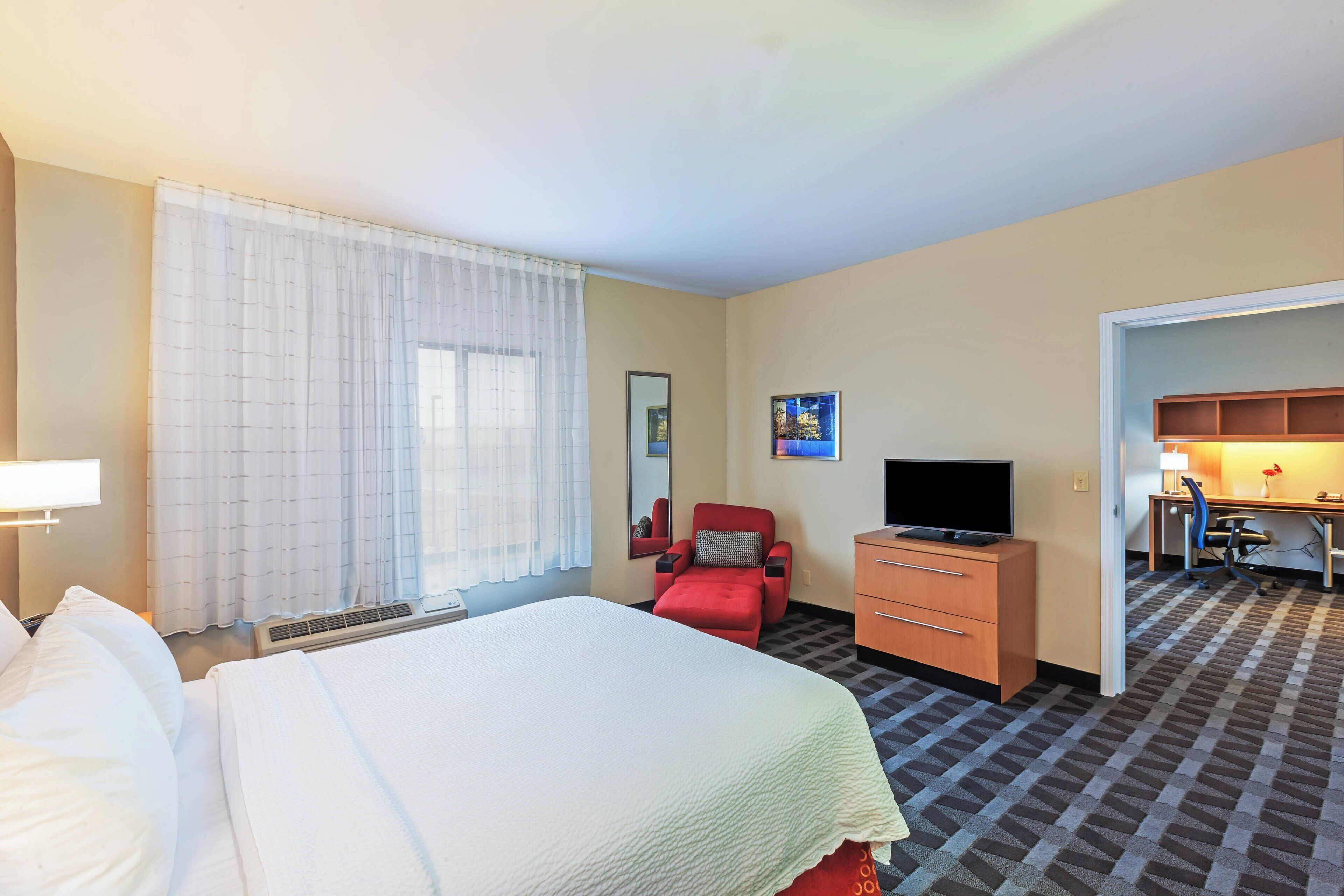 A hotel room with a bed, a desk, a chair, a television, and a bathroom visible through an open door.