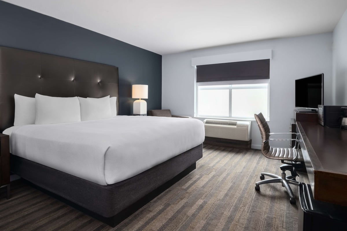 A hotel room with a large bed, a desk with a chair, a TV, and a window with blinds.