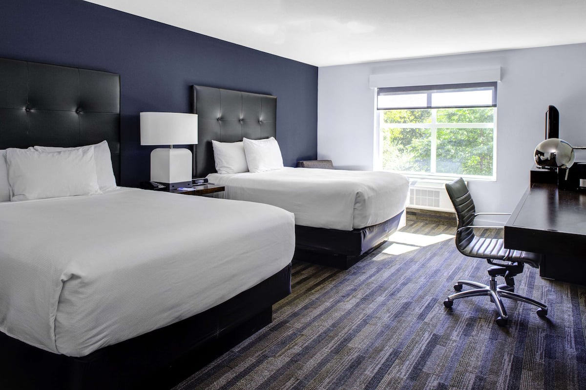 A hotel room with two beds, a desk, and a chair.