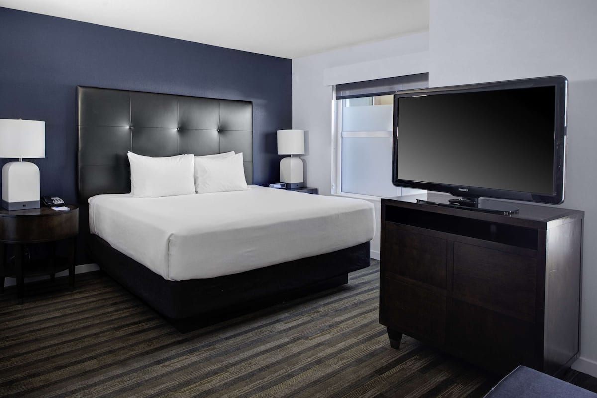 A hotel room with a large bed, a dark headboard, a flat-screen TV, and a wooden dresser.