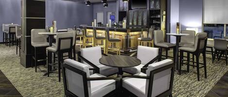 A modern bar area with high stools and a central round table, surrounded by bar chairs.