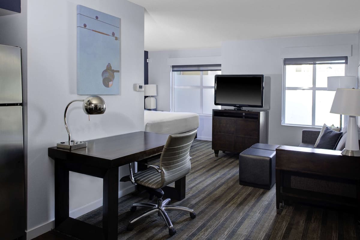 A hotel room with a bed, a desk with a lamp, a TV, a chair, and a sofa.