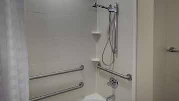 A bathroom with a shower, grab bars, and a white bathtub.