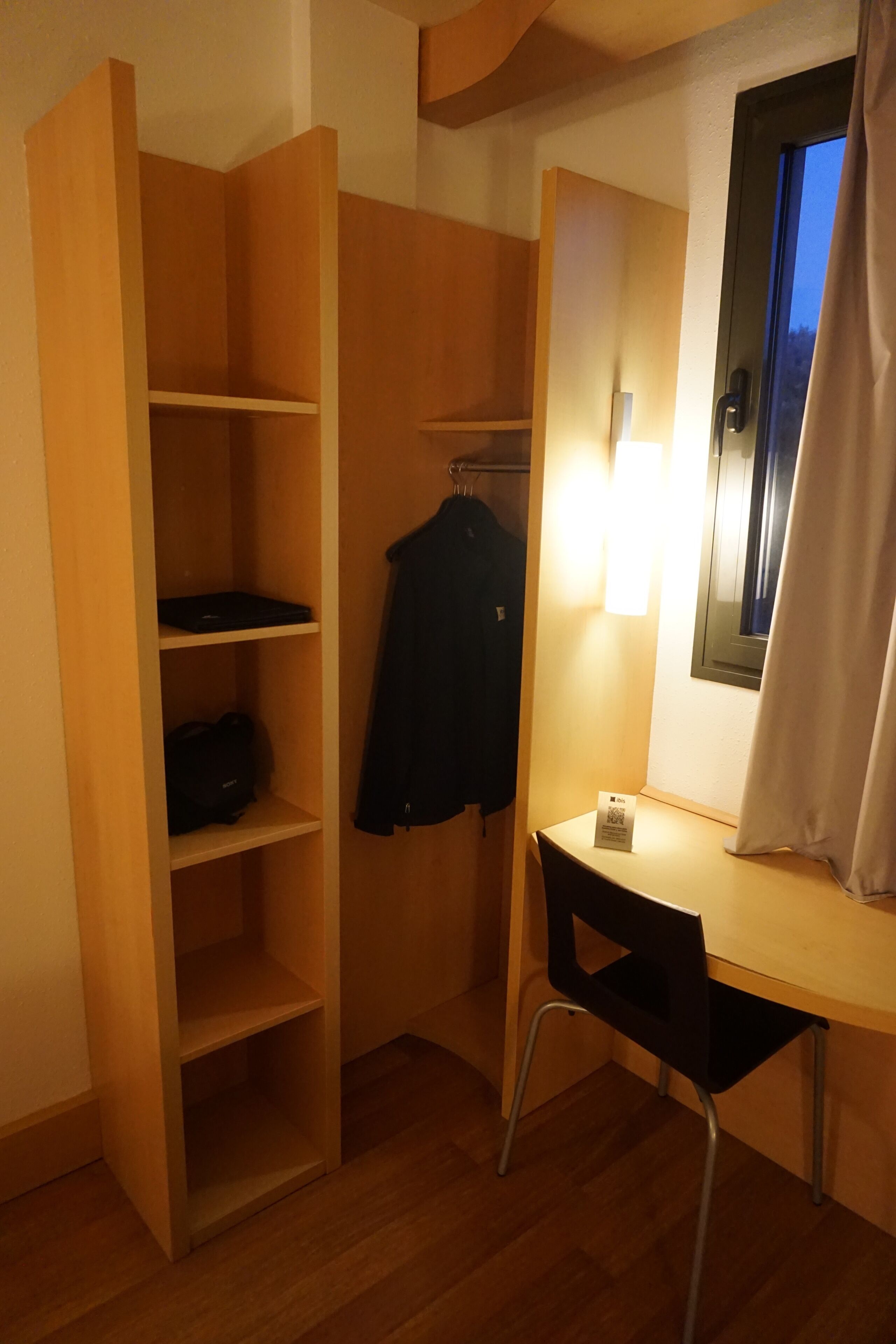 A compact room with a desk, chair, and shelving unit.