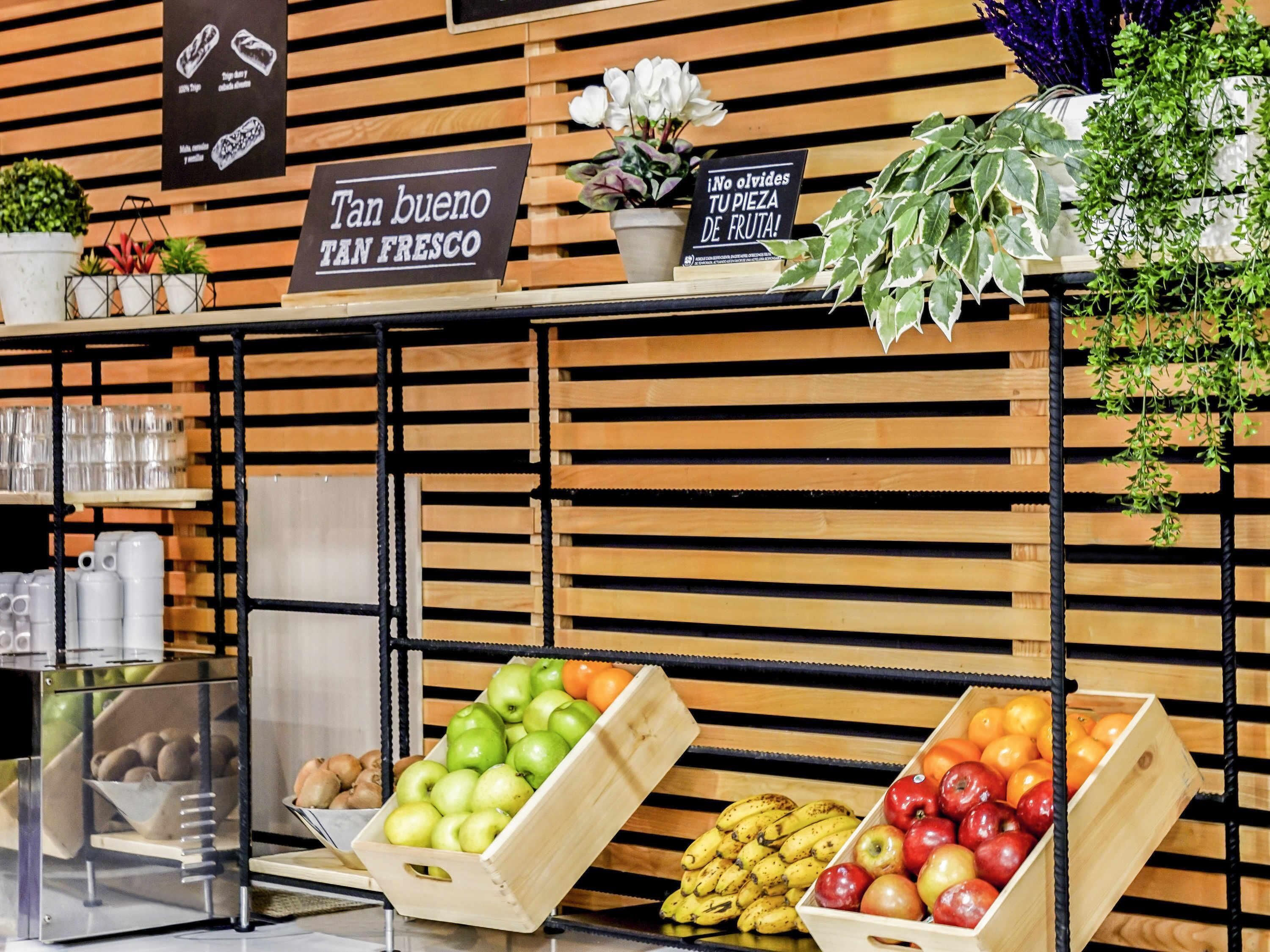 Una exhibición de frutas con cajas de madera, un letrero que dice 'Tan bueno TAN FRESCO' y otro que indica '¡No olvides tu compra de fruta!'