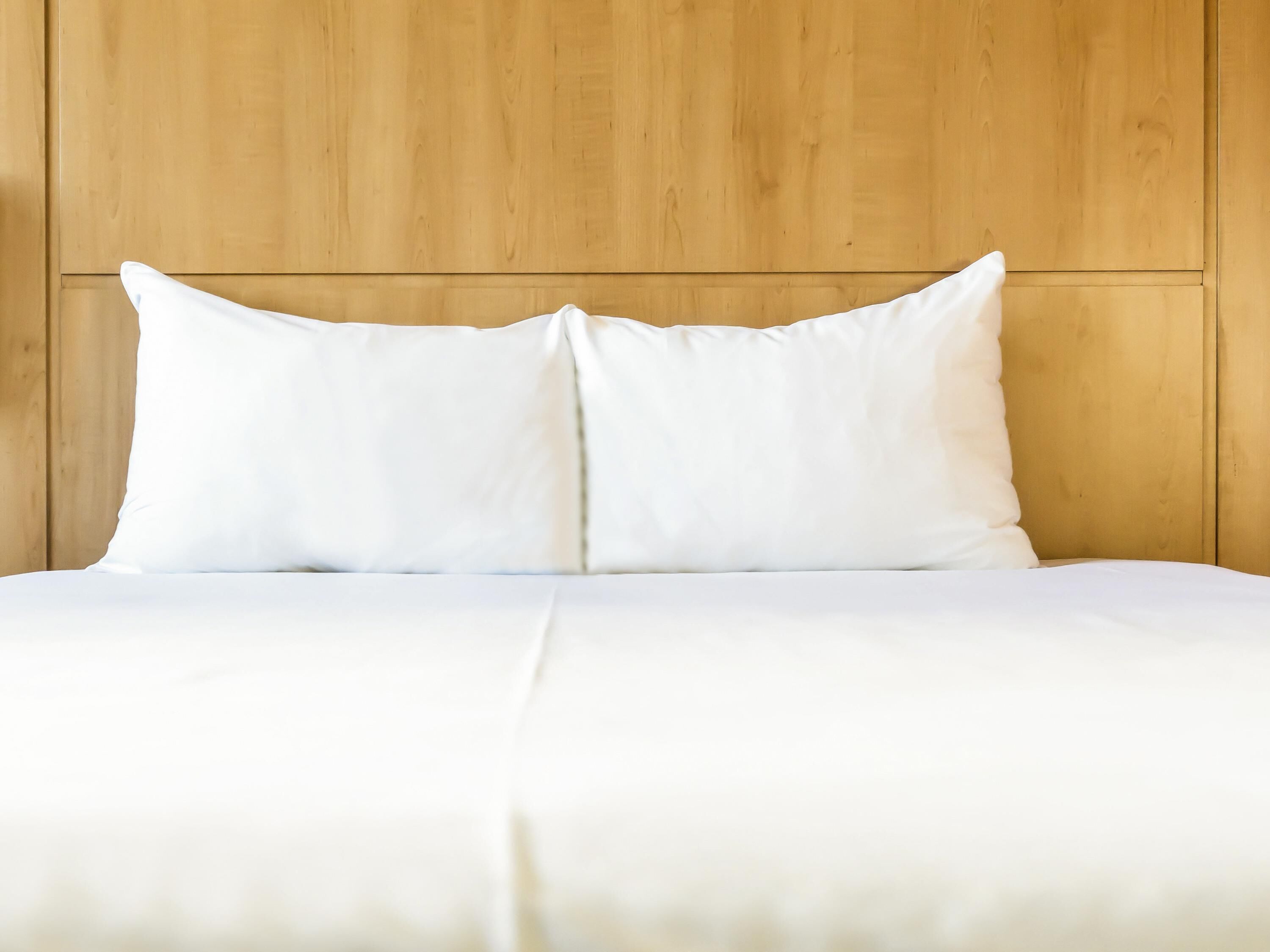 A bed with white bedding and pillows against a wooden headboard.