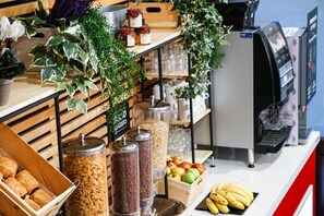 A breakfast bar with jars of granola, a fruit basket, and a coffee machine.