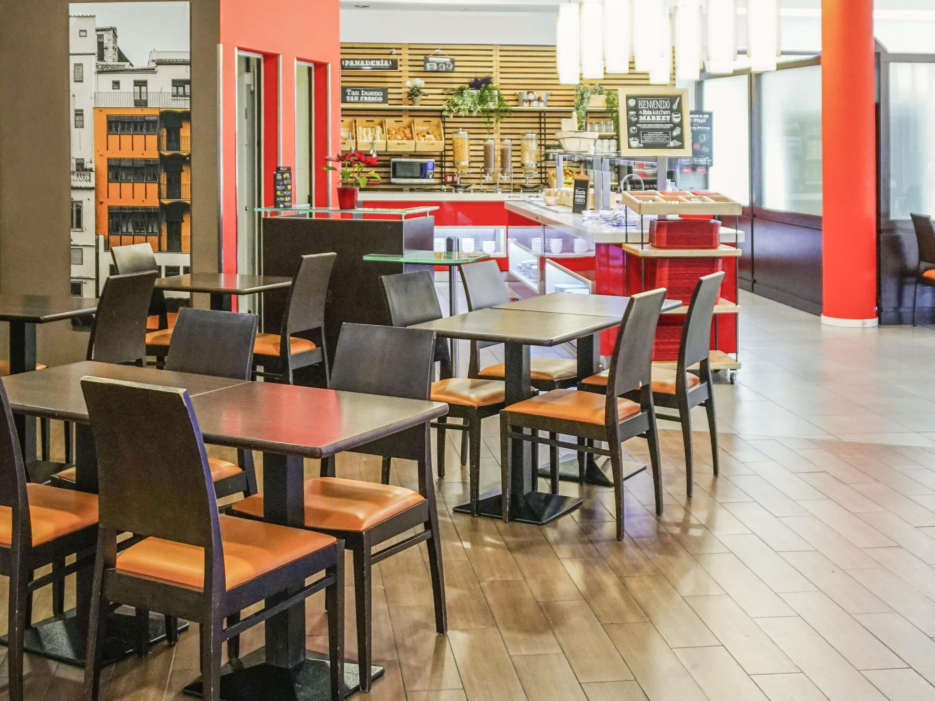 Una cafetería con mesas y sillas, una barra con productos horneados y un cartel dando la bienvenida a los visitantes.