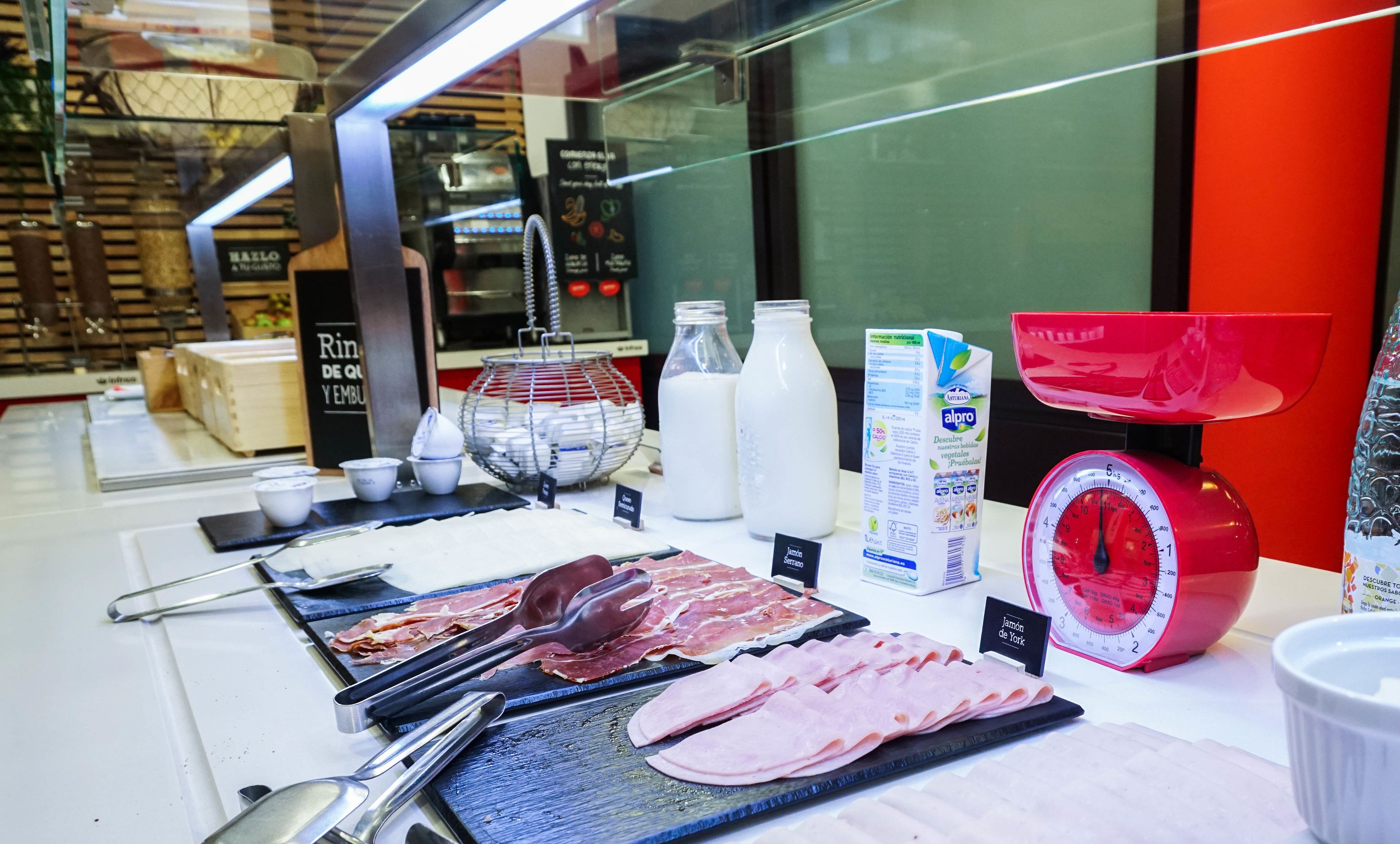 A deli counter with various meats, dairy products, and a weighing scale.