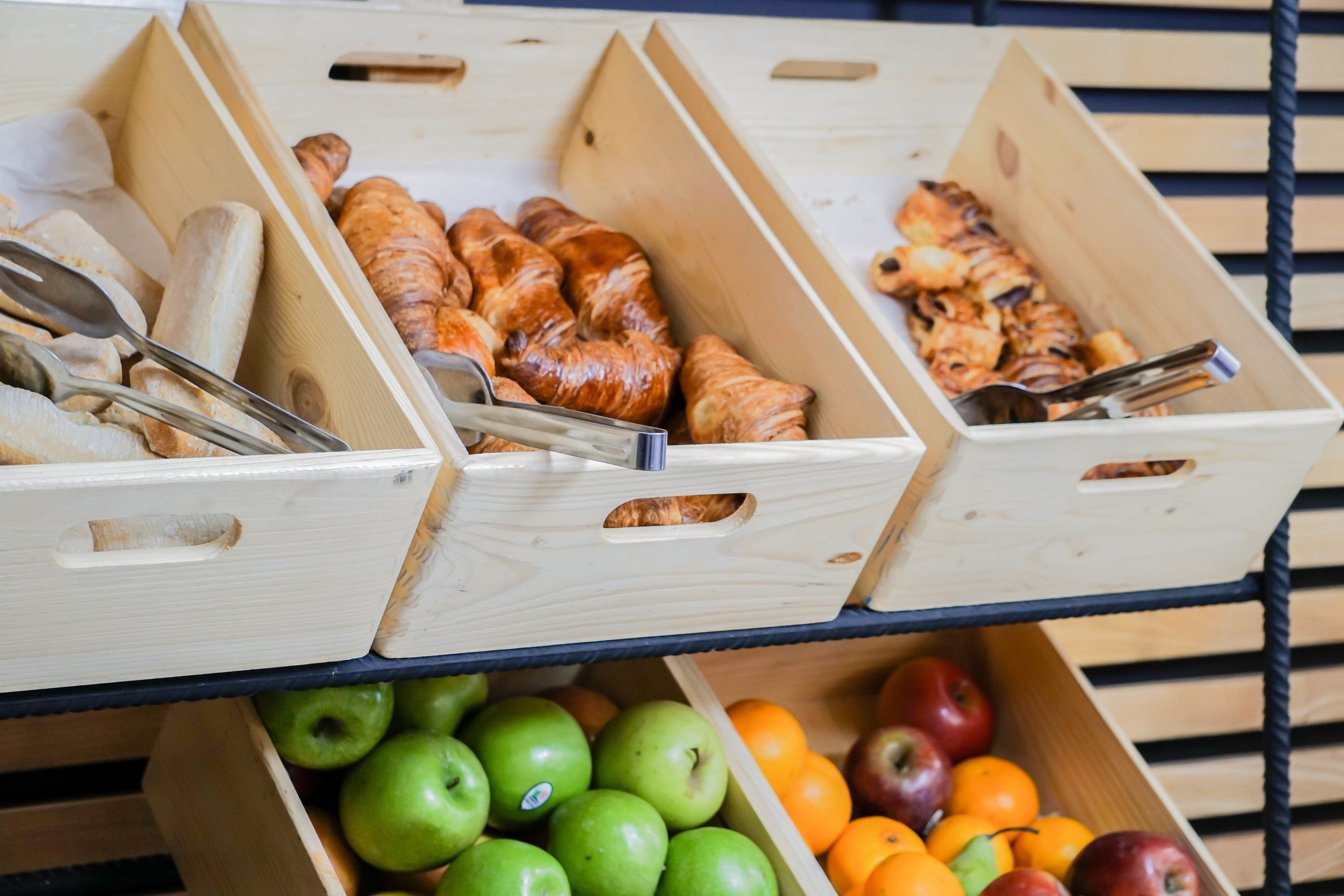 Three wooden crates on a shelf, each containing different food items like apples, oranges, and pastries.