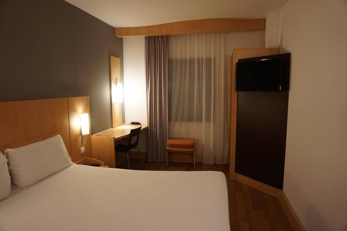 A hotel room with a bed, a desk, a chair, a television, and a window with curtains.