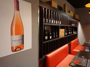 A wine cellar with shelves of bottles, a large wine bottle poster, and orange seating. - ibis Girona Costa Brava (Girona)