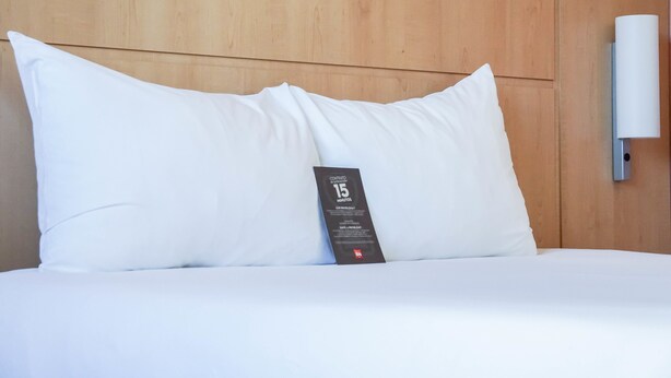 Una cama bien tendida con una almohada blanca y un control remoto encima.