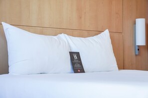 Una cama bien tendida con una almohada blanca y un control remoto encima.