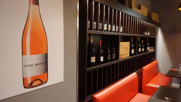Una bodega con estantes llenos de botellas, un cartel grande de una botella de vino y asientos color naranja.