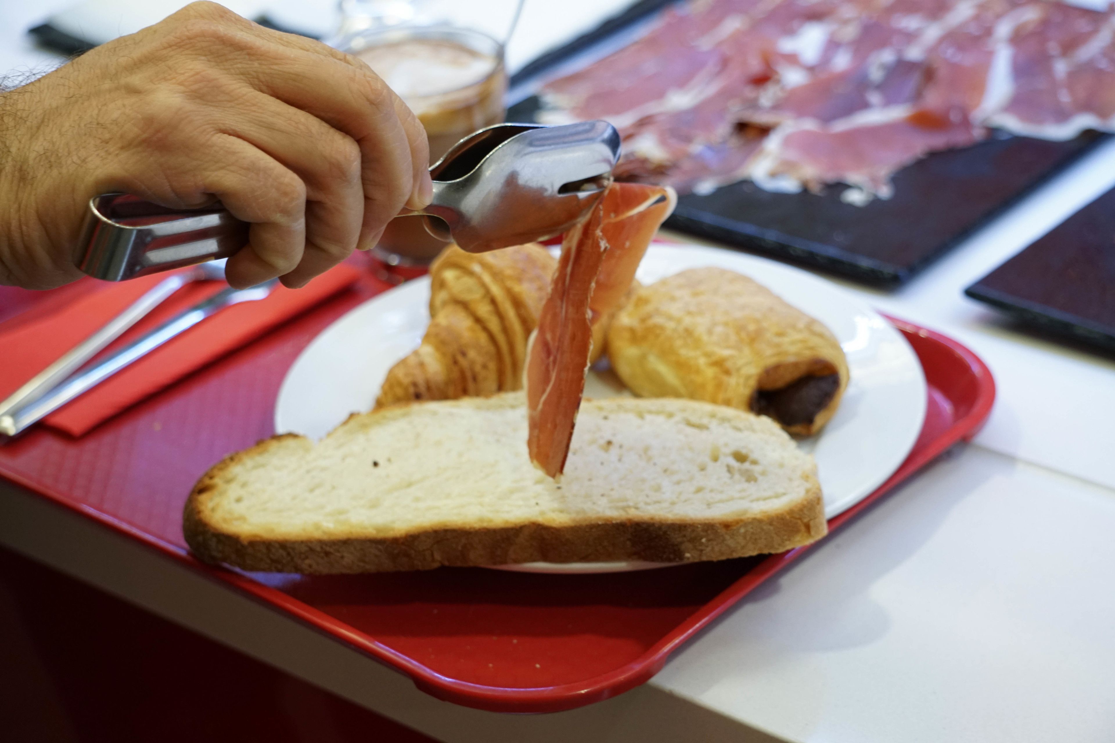 Une main utilise une trancheuse à viande pour couper du jambon sur une tranche de pain.
