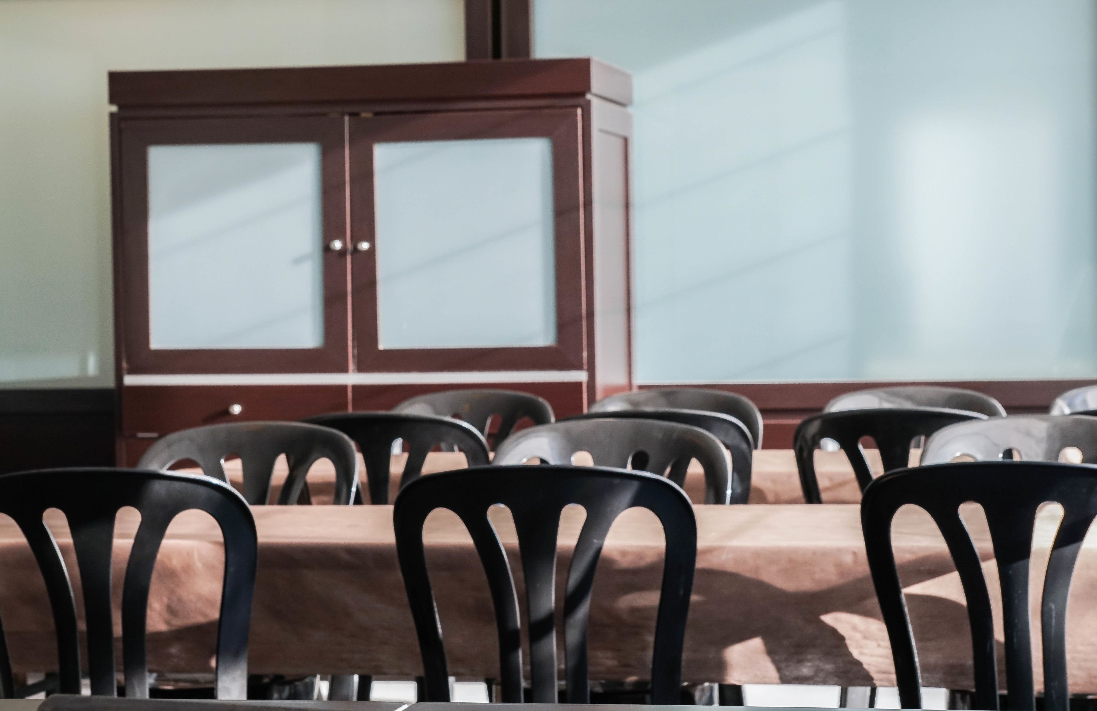 Un salón de conferencias con una mesa marrón, sillas negras y un mueble de madera con puertas de vidrio.