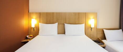 A hotel room with a large bed, two bedside tables, and wall-mounted lamps.
