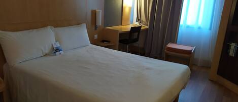 A hotel room with a large bed, a desk, a chair, and a small table.