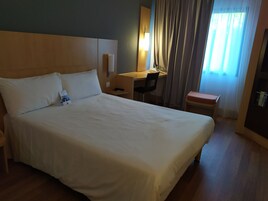 Una habitación de hotel con una cama grande, un escritorio, una silla y una mesita.