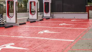 Three Tesla charging stations with red and white branding, set on a paved area with directional arrows.