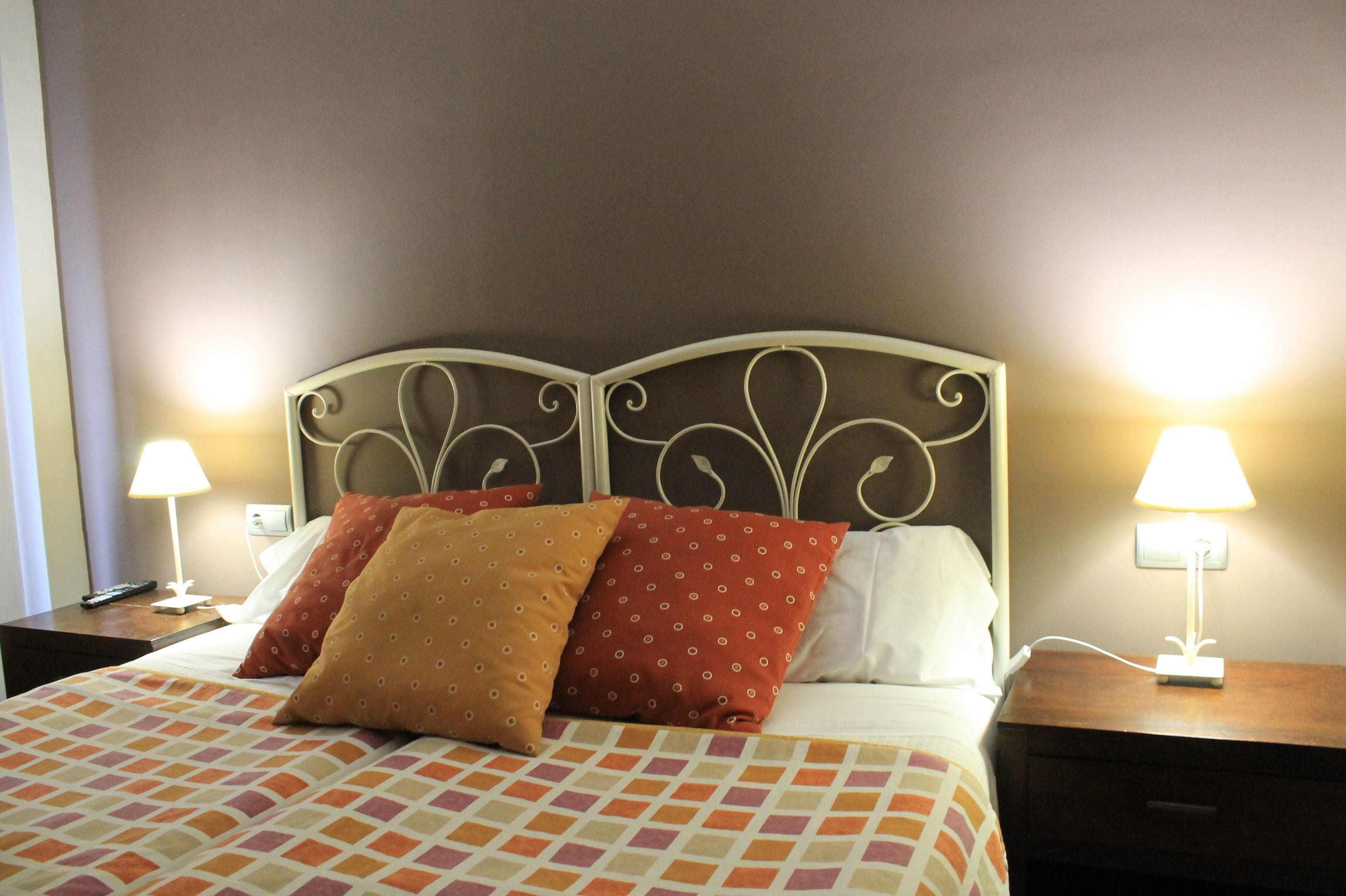 A neatly made bed with patterned bedding, two bedside lamps, and a wall-mounted nightstand.