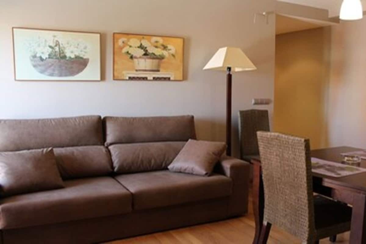 A living room with a brown sofa, a dining table with chairs, and two wall-mounted paintings.