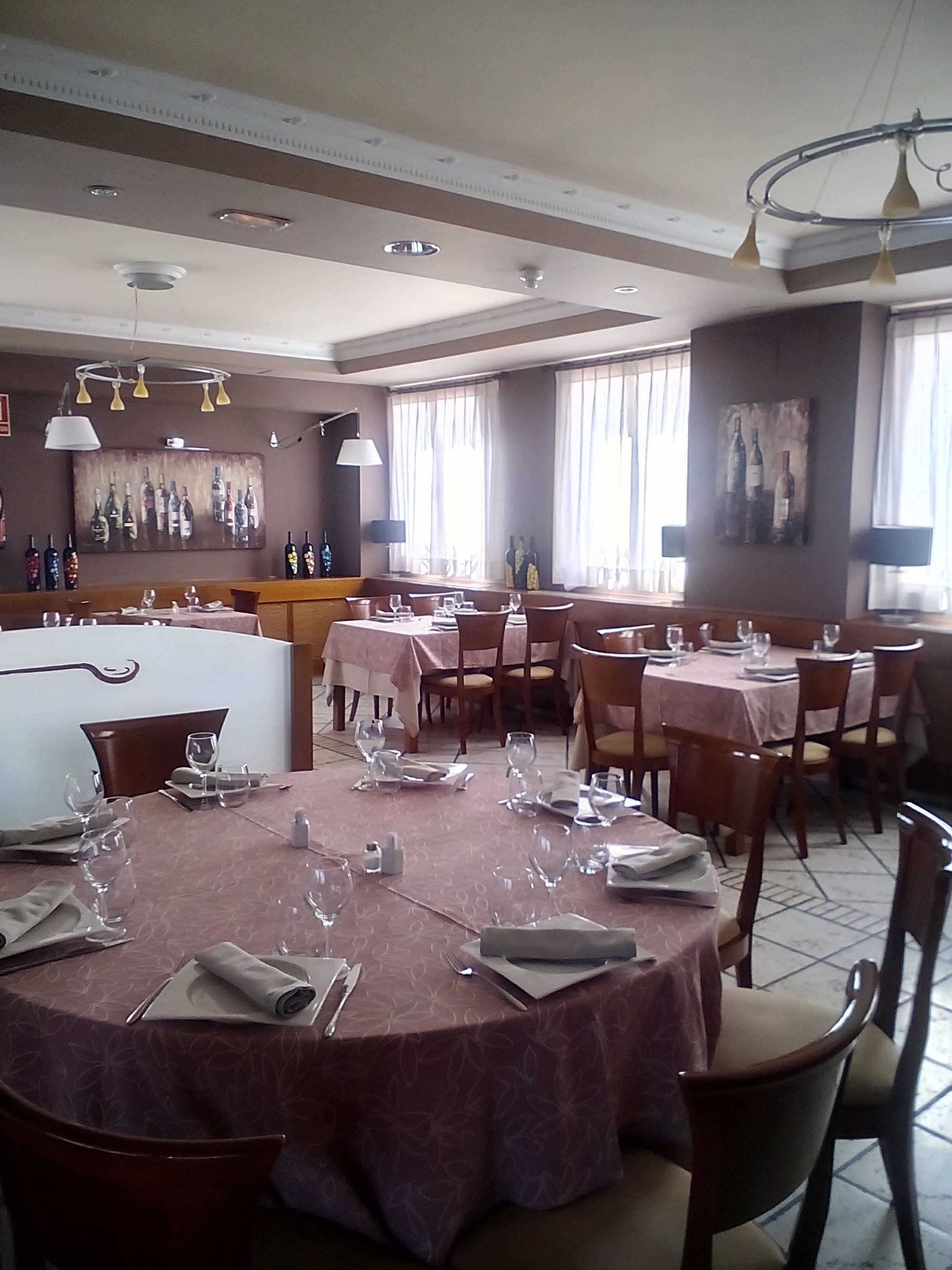 A restaurant with round tables set for dining, a bar area, and a wall with a wine bottle display.