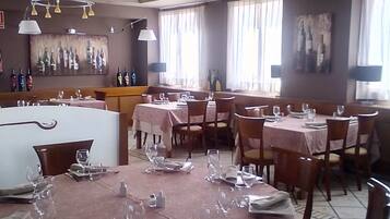Een restaurant met ronde tafels klaar voor het dineren, een bar en een wand met een wijnfles presentatie.