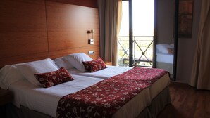 A double bed with a floral bedspread and two pillows, a nightstand, a wall-mounted lamp, and a balcony with a view of a building. - El Tollo Hotel (Utiel)