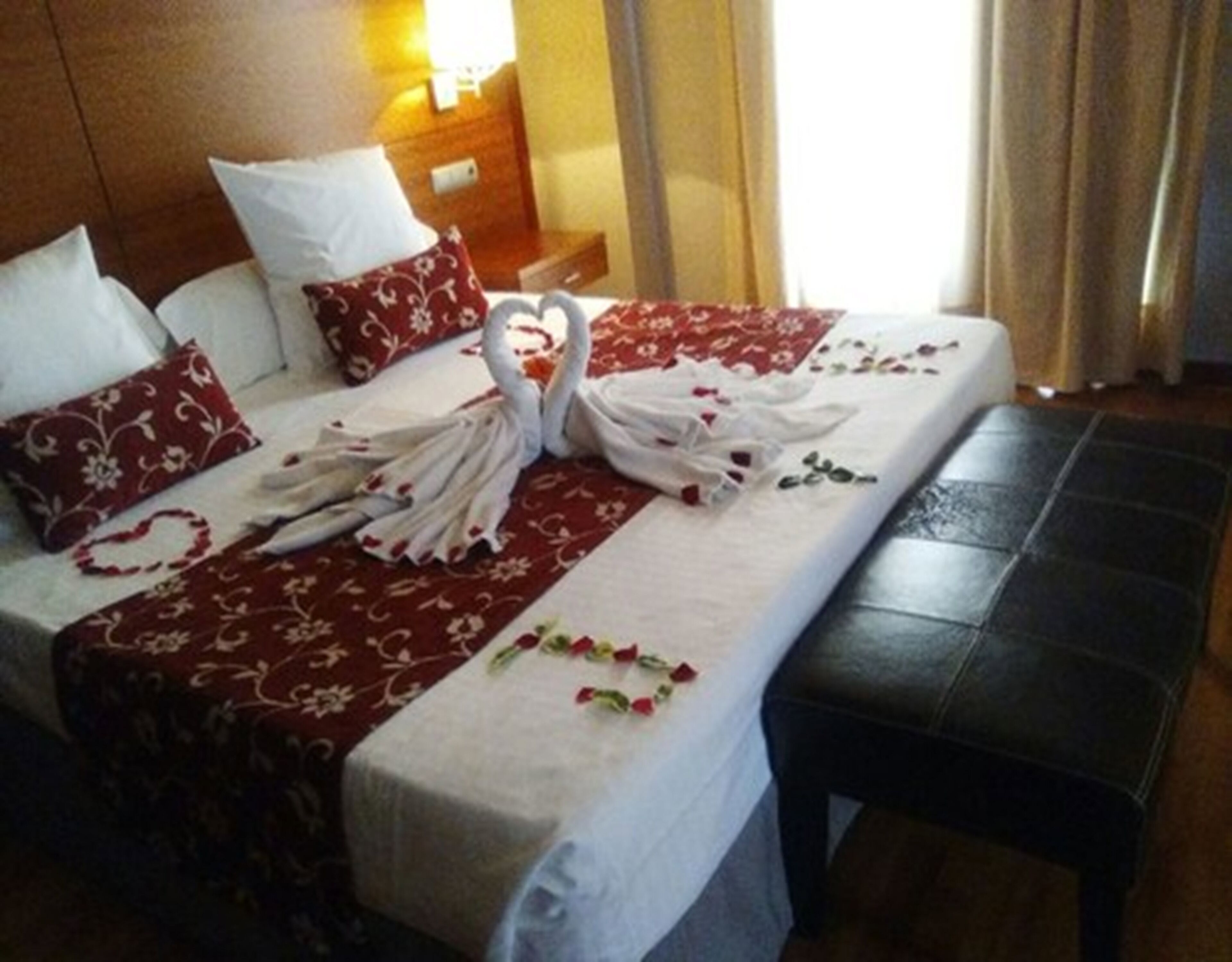 Una habitación de hotel con una cama decorada con una composición de toallas con forma de cisne y almohadas estampadas con motivos florales rojos.