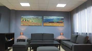 Un salon moderne comprenant un canapé, un pouf et deux tables d’appoint, avec deux tableaux représentant des paysages accrochés au mur.