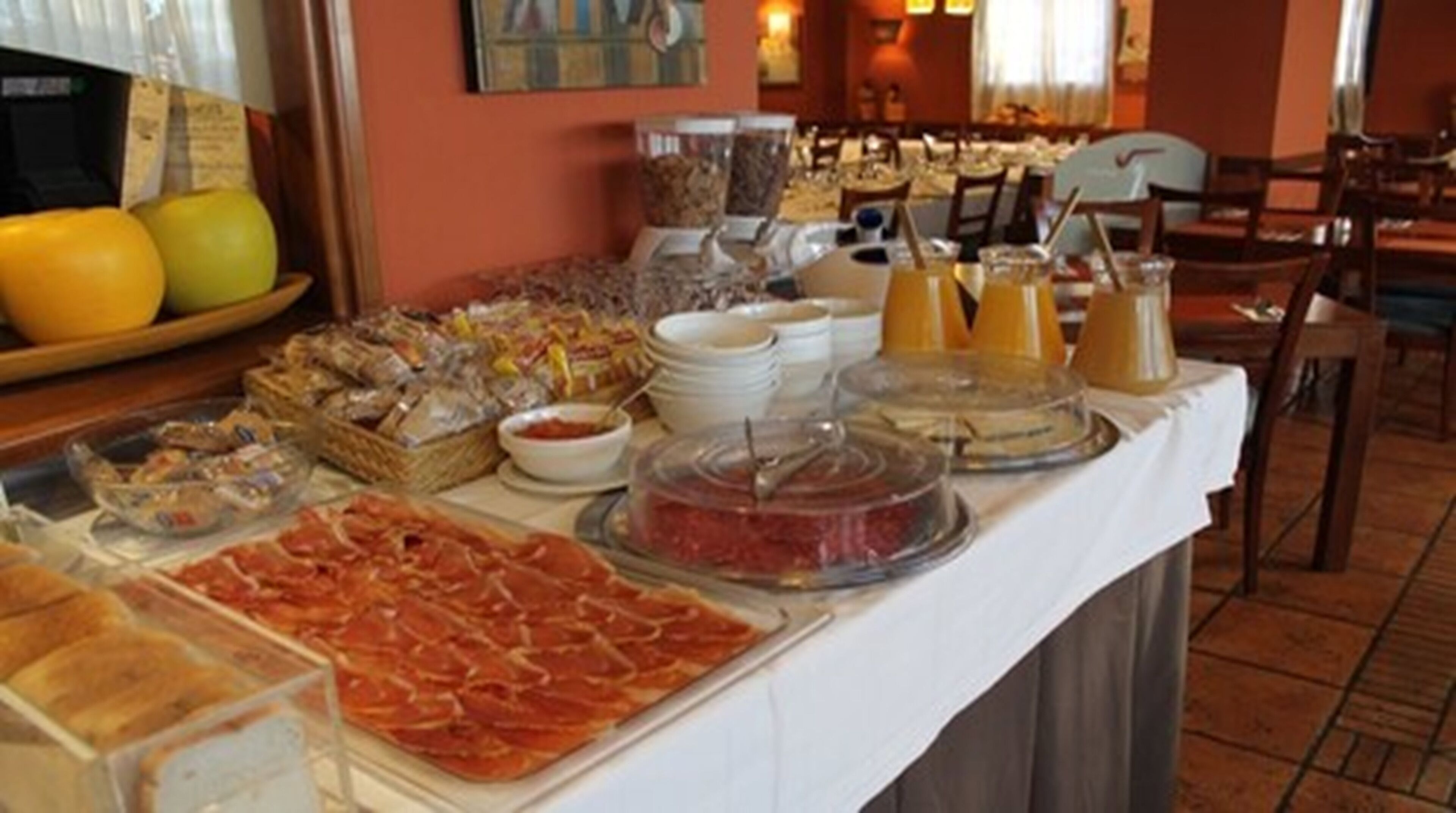 Una mesa de buffet con diversos alimentos, entre ellos carnes, quesos y frutas.
