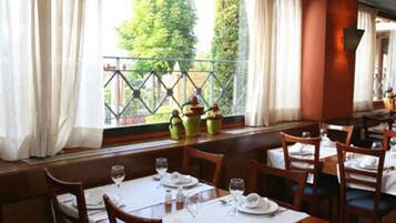 A dining area with tables set for two, a view of the outdoors through a window, and a railing outside.