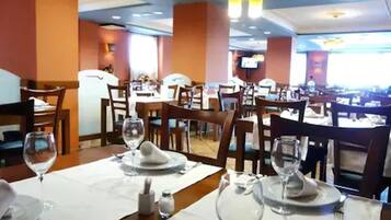 Un restaurante con mesas dispuestas para comer, sillas y una pantalla de televisión al fondo.