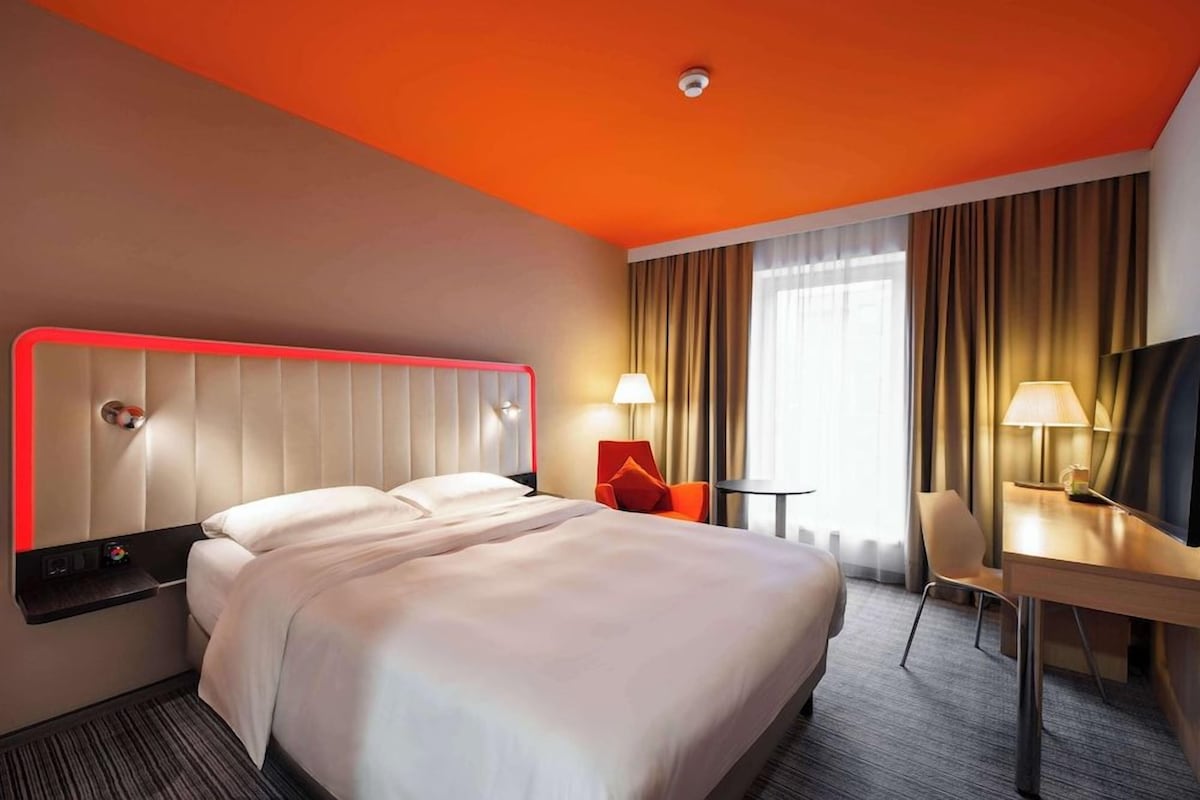 A hotel room with a large bed, a desk, two chairs, and a TV.