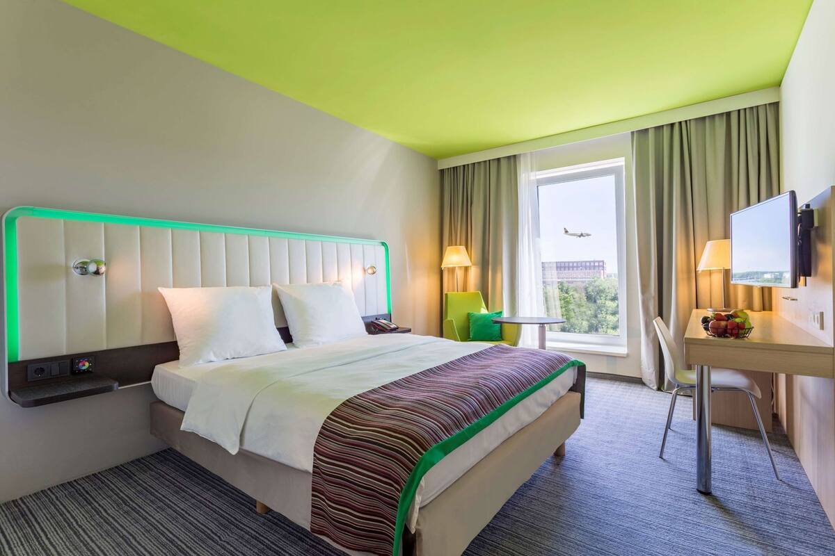 Een hotelkamer met een bed, nachtkastje, bureau, stoel en een raam met uitzicht.