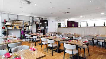 Un restaurante moderno con varias mesas y sillas, una zona de cocina y ventanas amplias.