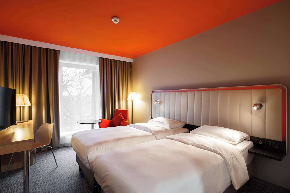 Een hotelkamer met twee bedden, een bureau, een stoel en een raam met gordijnen.