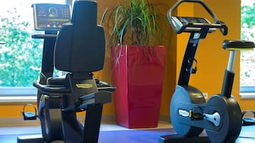 A stationary bike and an elliptical machine in a room with a large window, a red planter with a plant, and a digital display on the bike.