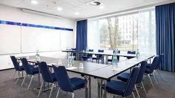 Un salón de conferencias con una larga mesa, sillas azules y amplias ventanas con cortinas.