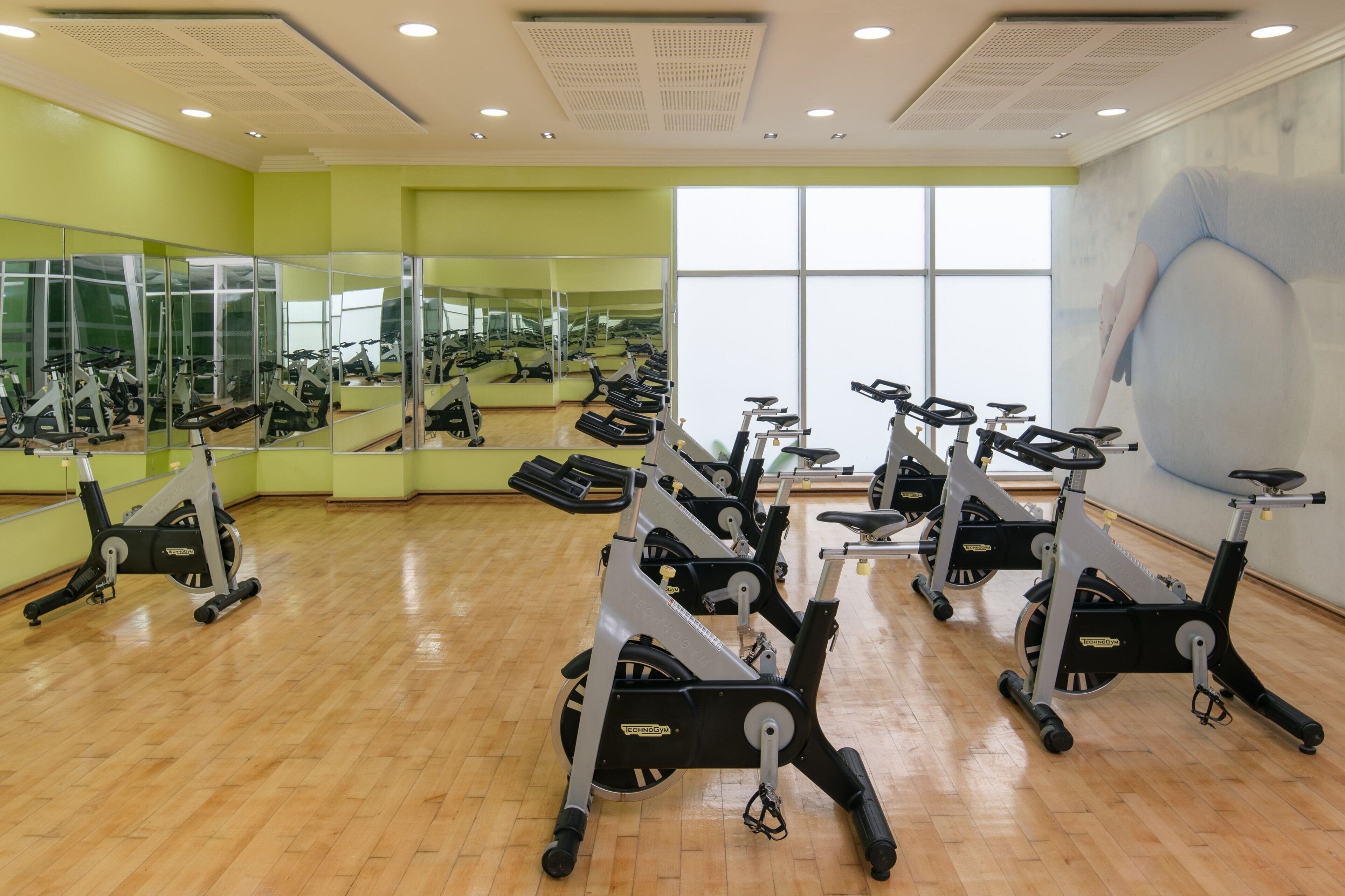 A gym with stationary bikes, mirrors, and a large window.