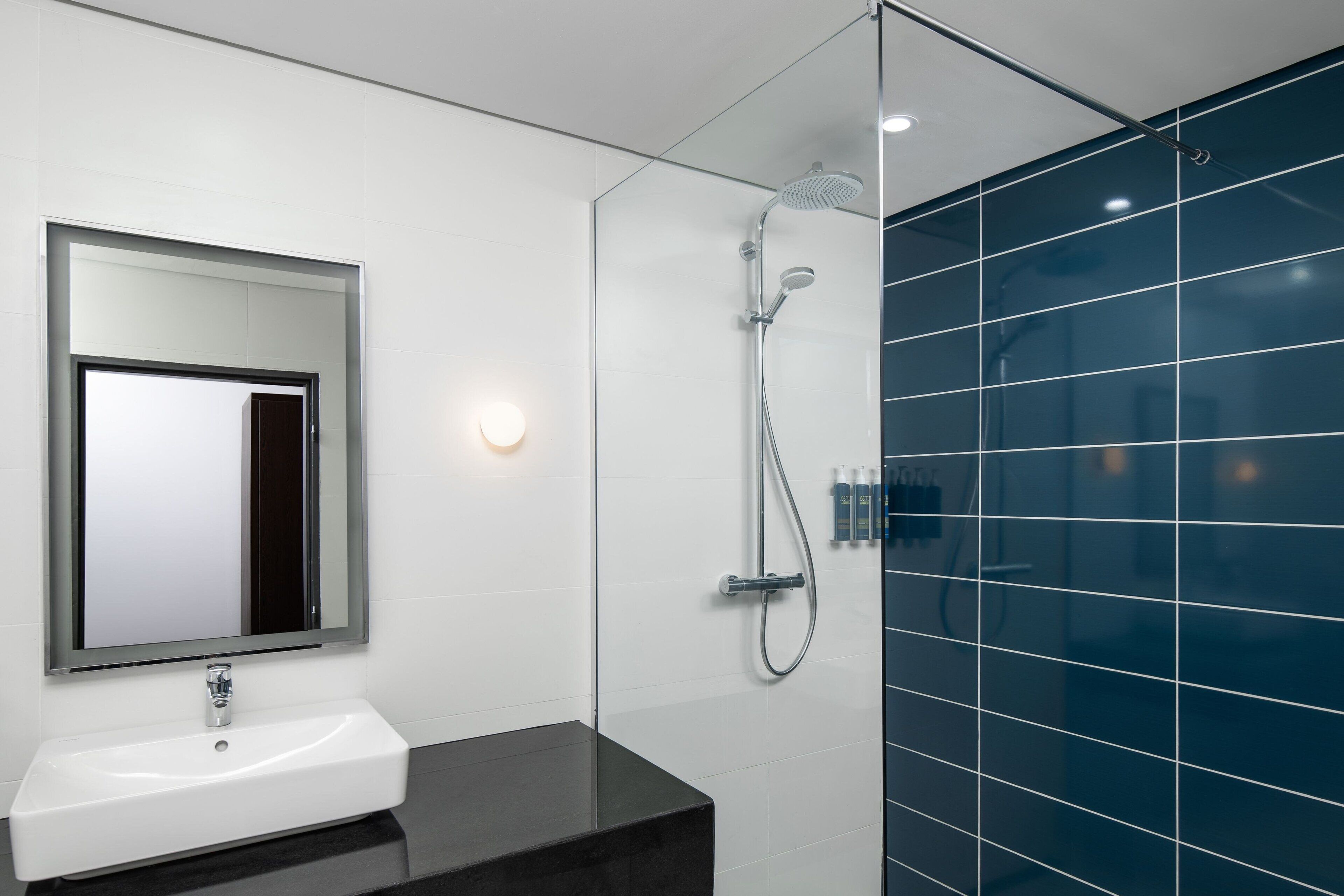 A modern bathroom with a white sink, a large mirror, a glass-enclosed shower, and blue-tiled walls.